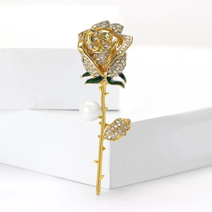 Elegant gold rose brooch with sparkling rhinestones and a white pearl on a clean white base