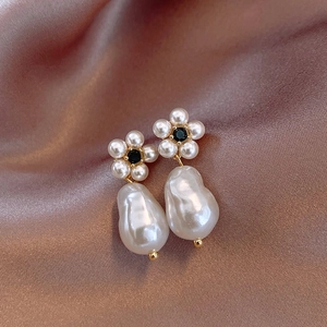 Detailed macro of Baroque pearl earrings with golden floral black gemstone accents