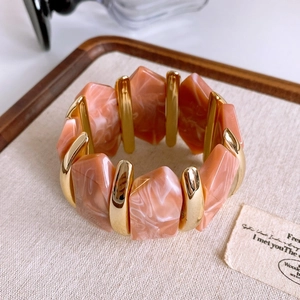 Macro shot of pink marble resin tiles and golden metal spacers on elastic bracelet