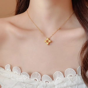 Detailed close-up of a gold hollow clover pendant necklace with zircons on a model's neck
