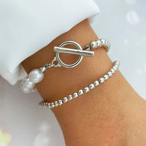 Close-up of layered silver chain bracelets with white pearls and a classic T-bar toggle clasp