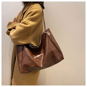 Detail view of large dark brown oil wax leather tote bag worn by model with camel coat