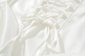 Detailed close-up of white satin dress featuring elegant corset lacing and silky texture