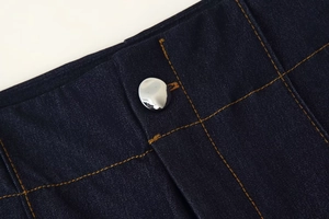 Détail d'une veste en jean bleu foncé avec coutures jaunes et bouton métallique argenté