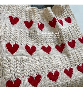 Detalle de textura de punto trenzado en bolso beige con patrones de corazones
