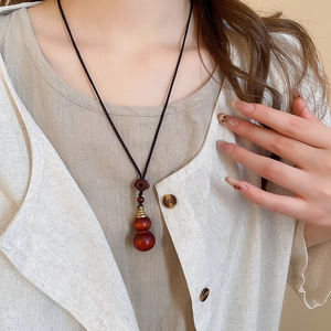 Detailed view of dark red wood gourd pendant on a black cord necklace with natural grain