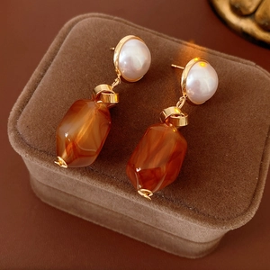 Detailed shot of amber resin earrings with pearls on a brown velvet jewelry box