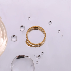 Macro shot of gold stainless steel ring with scale texture on a reflective water surface