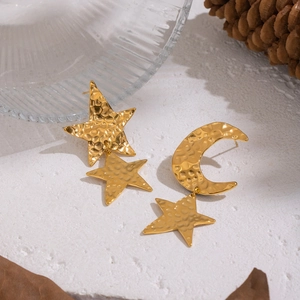 Detailed view of asymmetric gold hammered star and moon earrings on a rustic white base