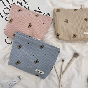 Flat lay of pink, beige, and blue corduroy makeup bags with bear patterns on white fabric