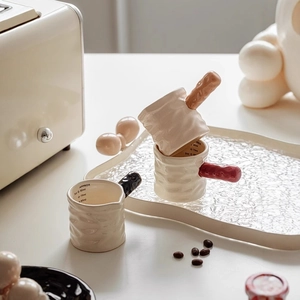 Ceramic coffee creamer set with handles and measurement markings in a kitchen setting