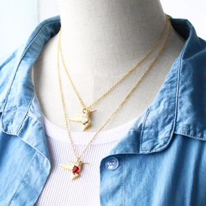 Detail view of two gold hummingbird necklaces with red and white heart-shaped zircon stones