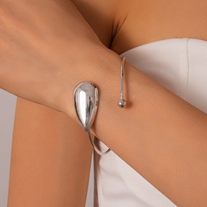 Gros plan du bracelet ouvert argenté poli avec goutte d'eau et texture métallique lisse
