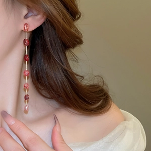 Detail of long strawberry crystal tassel earrings with gold chain on model's ear