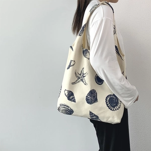 Detail of a large canvas shoulder bag with blue starfish print worn by a model
