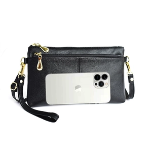 Close-up of black litchi texture crossbody bag with gold zippers and smartphone for scale
