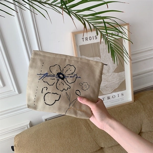 Detailed close-up of beige canvas cosmetic bag with black floral embroidery and zipper