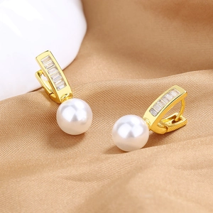 Macro shot of geometric gold earrings with rectangular zircon and elegant white pearl