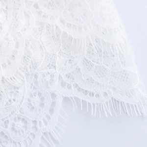 Gros plan sur une robe en dentelle blanche avec texture florale et bordure cils