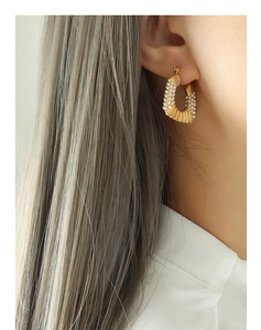 Detail of C-shaped gold hoop earrings with ribbed texture and white bead inlay on model