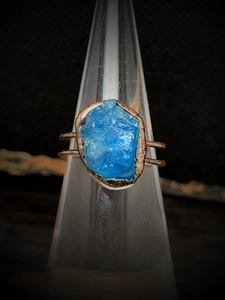 Close-up of a raw blue birthstone ring on a cone display stand with copper finish