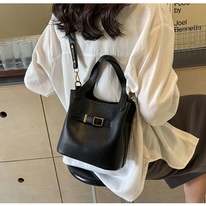 Lifestyle view of black pebbled leather bucket bag with metal buckle and shoulder strap