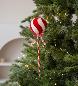 Detail of red and white candy cane ornament with a bow hanging on a lit Christmas tree
