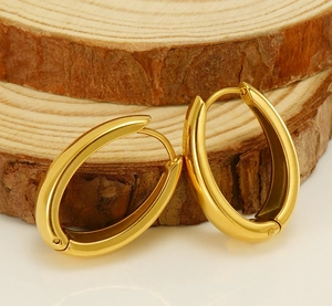 Boucles d'oreilles créoles ovales dorées polies sur un support en bois naturel