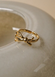 Macro shot of polished gold bow ring with adjustable opening on a minimalist stone base