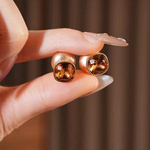Dettaglio degli orecchini geometrici in ambra con perla color crema e finitura dorata raffinata