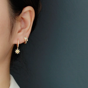 Close-up of gold-plated hoop earring with crystal sunburst pendant on female ear