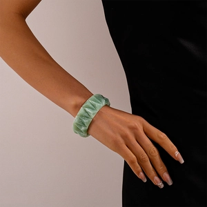 Close-up of a green geometric acrylic bracelet on a model wrist against a grey background