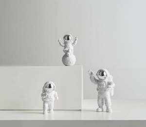 Three white and silver astronaut figurines set on minimalist geometric display stands