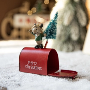 Red Christmas mailbox ornament with cartoon figure and snowy pine tree on white snow