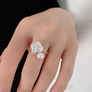 Detail of hand wearing a gold beaded ring with a baroque pearl and a round white pearl