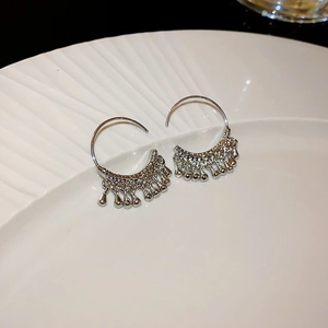 Macro detail of silver bohemian hoop earrings with beaded tassels on white plate