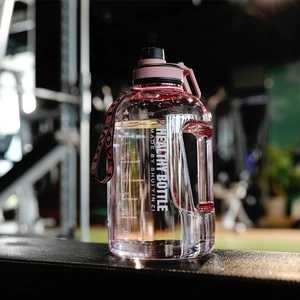 Close-up of pink sports water bottle with time markings and ergonomic handle in a gym
