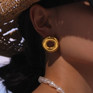 Golden hollow donut earrings with high-polish mirror finish shown on a model in sunlight