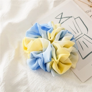 Detailed shot of a blue and yellow tie-dye chiffon scrunchie on a soft fabric background