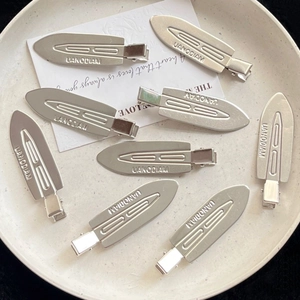 Macro detail of silver metal duckbill hair clips with brand logo on a display tray