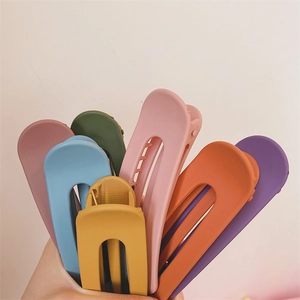 Matte finish duckbill hair clips in vibrant colors held in hand against pink background