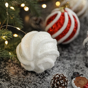 Rot-weiße Weihnachtsbaumkugeln und weiße Glitzer-Ornamente auf einem Tannenzweig