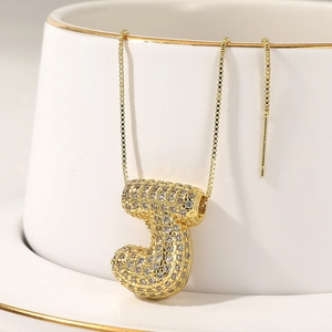 Close-up of golden bubble letter J pendant with shiny rhinestones on a box chain necklace