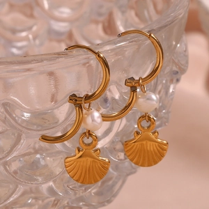 Close-up of gold earrings with freshwater pearls and shell charms on glass bowl