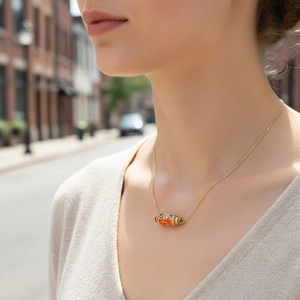 Detail of model wearing a gold chain necklace with an orange and blue enamel evil eye pendant