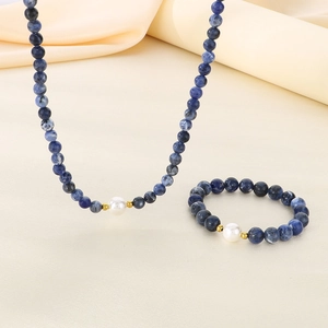 Detail view of blue beaded necklace and bracelet set with white pearl on silk fabric