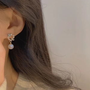 Close-up of elegant gold earrings with blue-grey opal, zircon leaves, and hanging pearls