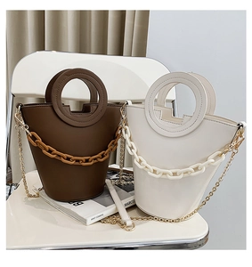 Detail of elegant handbags with circular handles and thick chain decor on a white chair
