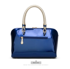Detail view of the back of a navy blue patent leather handbag with a gold zipper pocket
