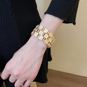 Detailed close-up of a wide golden bracelet with square metal plates and spiral textures